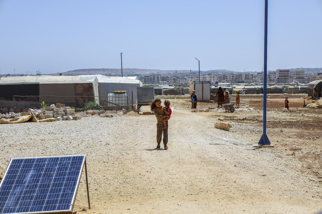 A young girl holds her brother in an camp for internally displaced persons in rural Idleb, Syria. Across the country, over 1.9 million IDPs have returned home since December 2024.